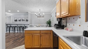 A modern kitchen with wooden cabinets, a stainless steel sink, and a bar area with stools. - Lakeside Paradise Escape/Jet Ski & Kayak Adventure (Dandridge)