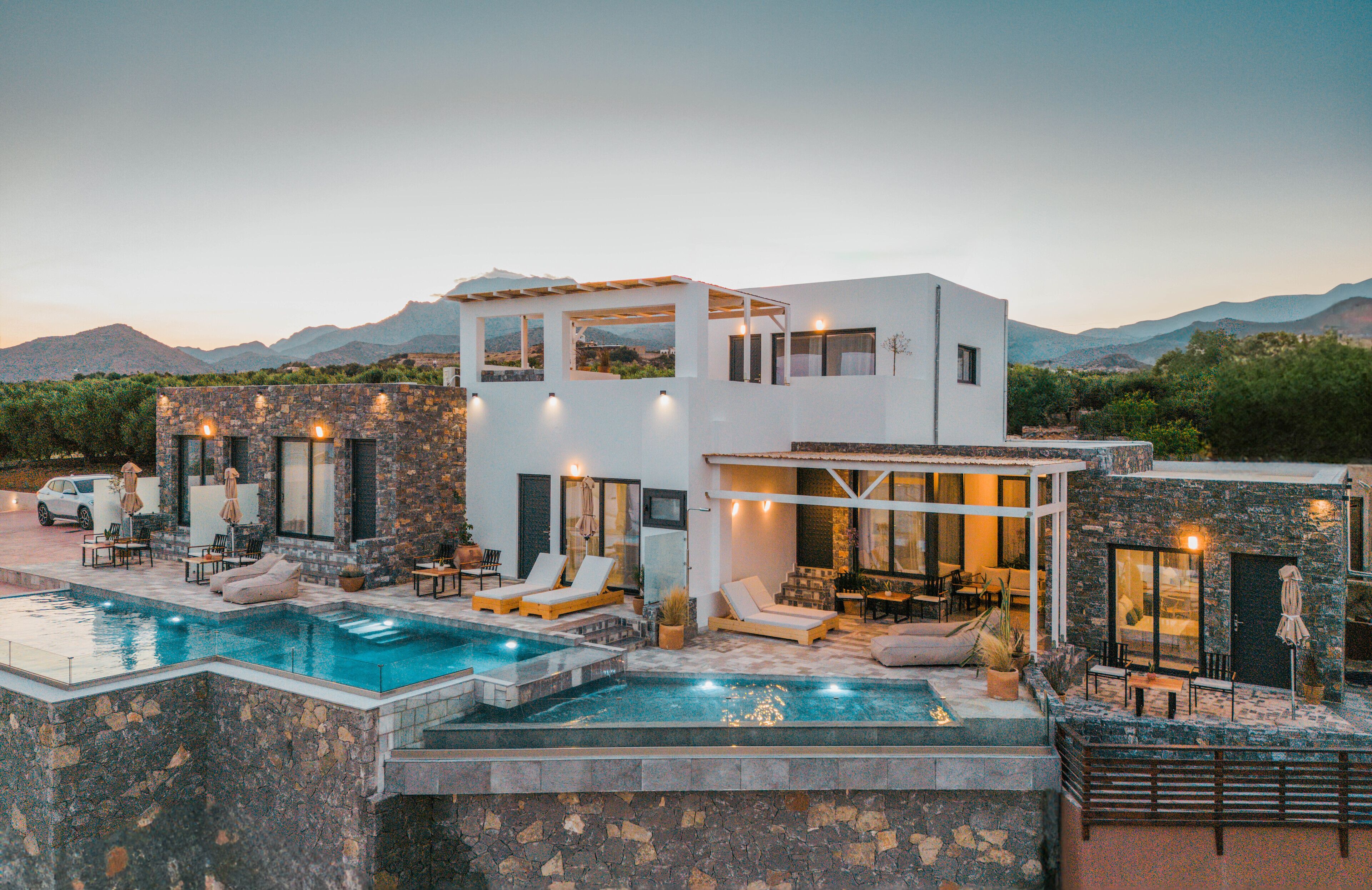 A modern house with a swimming pool, outdoor seating, and a view of mountains.