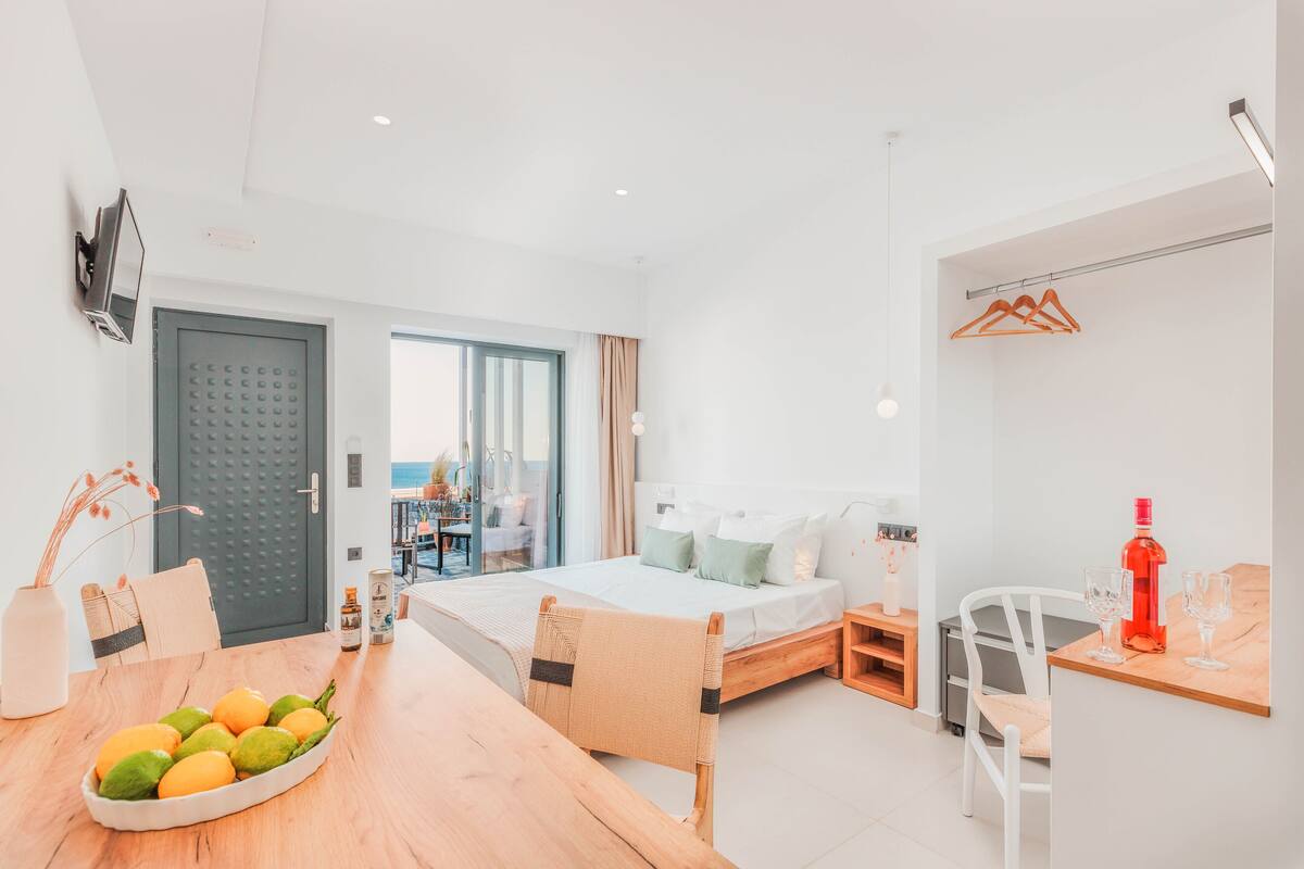 Een moderne hotelkamer met een bed, een eettafel met fruit, een televisie en uitzicht op het landschap.