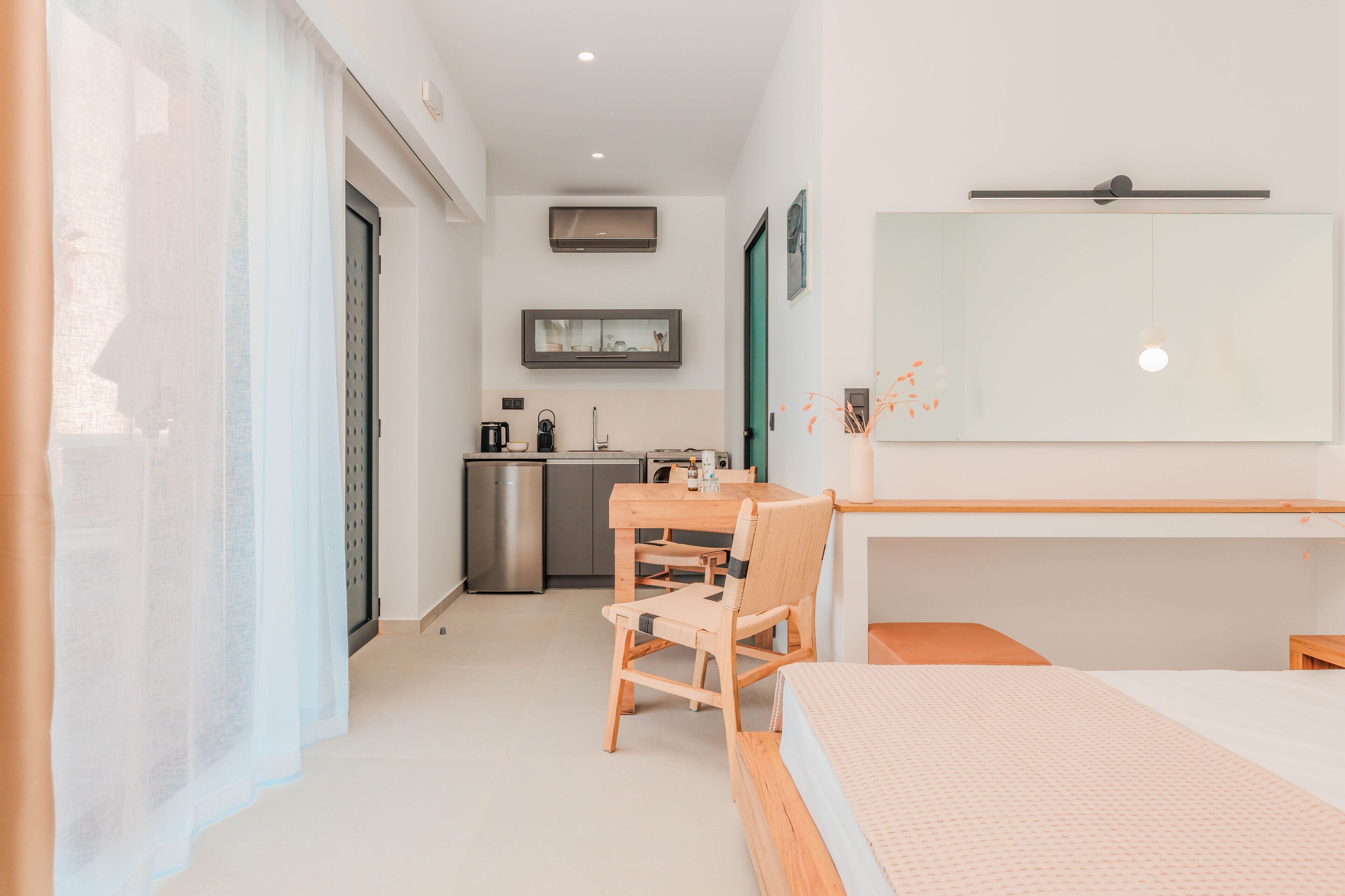 A compact hotel room with a bed, a small desk, a chair, a kitchenette, and a bathroom.