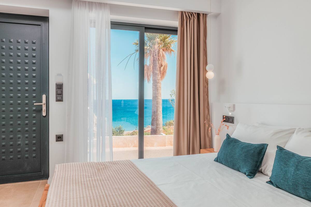 Een hotelkamer met een bed, uitzicht op zee en een schuifdeur.