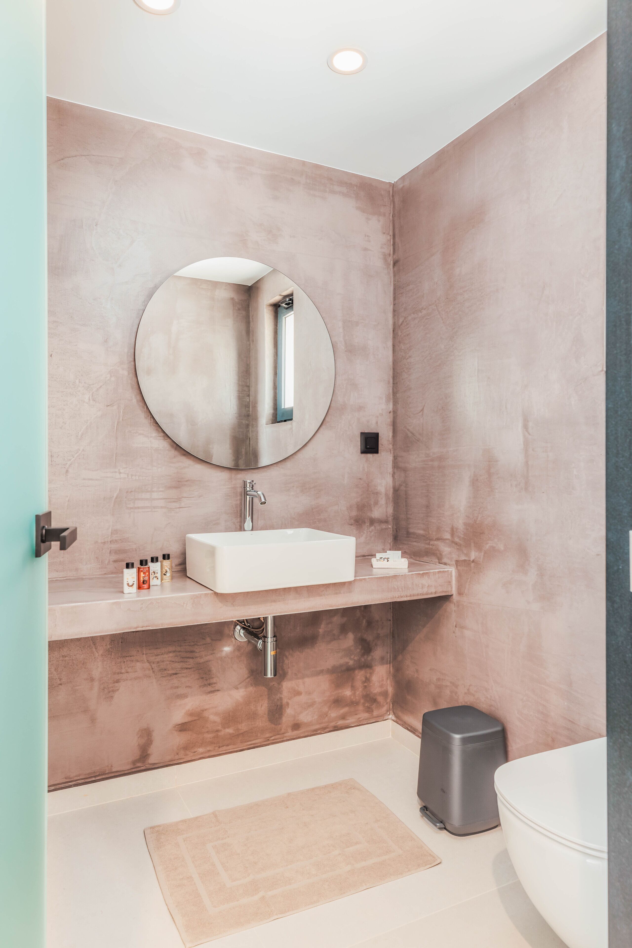 A modern bathroom with a round mirror, white sink, and a beige rug on the floor.