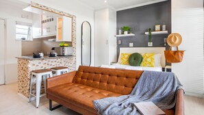 A modern living room with a brown sofa, a small kitchen area, and a dining table.