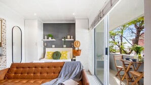 A modern living room with a brown sofa, a small table, and a balcony with wooden chairs.