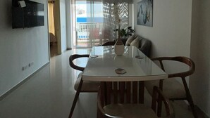 A modern dining area with a glass table, wooden chairs, and a flat-screen TV mounted on the wall. - Rodadero Excalibur 8c (Santa Marta)