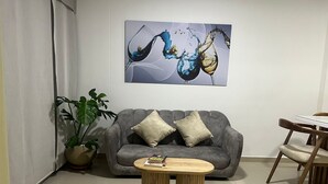 A living room with a grey sofa, two round wooden coffee tables, a potted plant, and a painting of abstract figures. - Rodadero Excalibur 8c (Santa Marta)