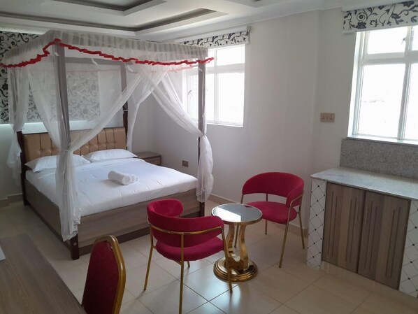 Un dormitorio con cama con dosel, una pequeña mesa redonda, dos sillas y una zona de kitchenette.