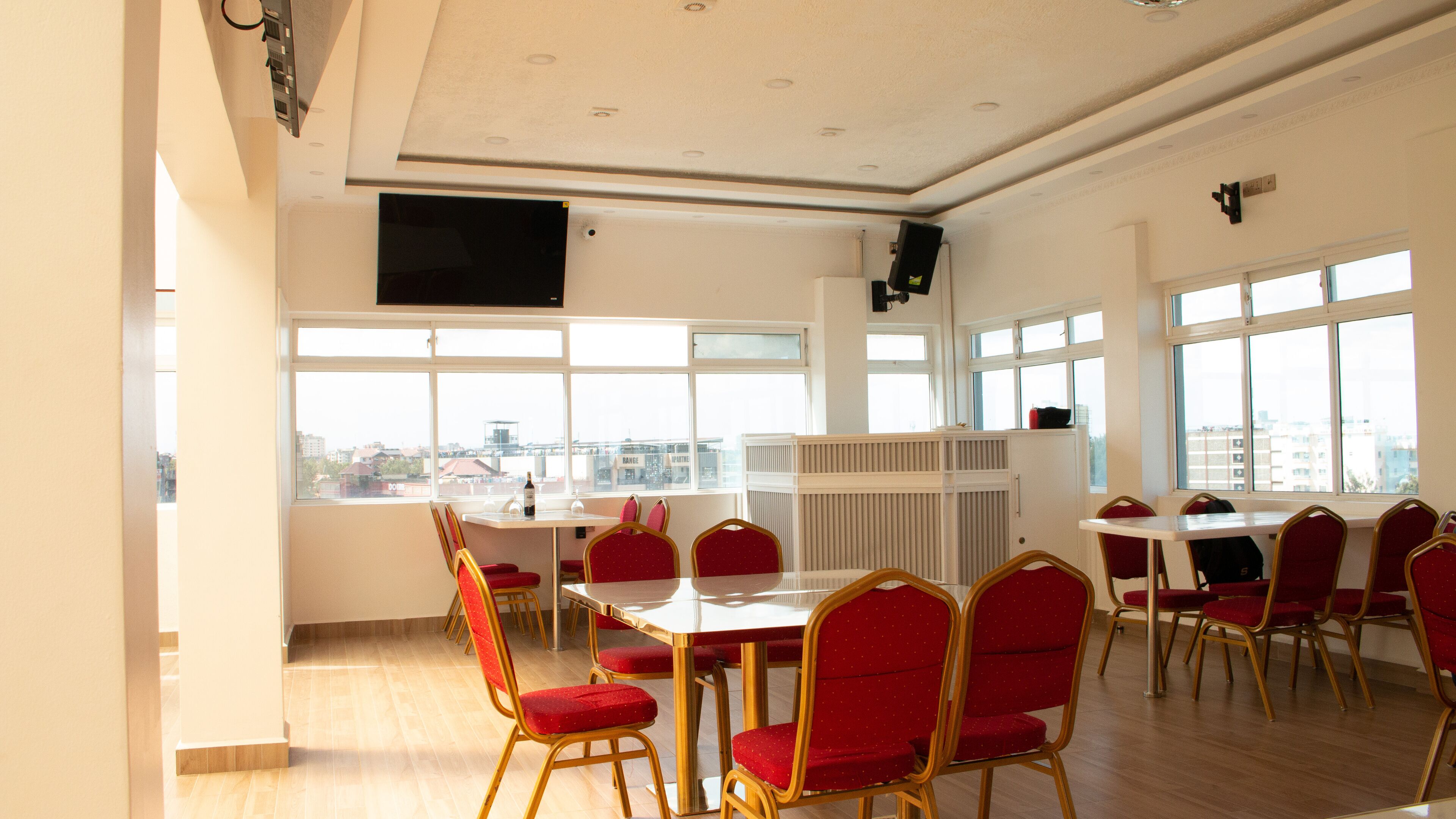 A conference room with a large table and red chairs, large windows with a city view, and a mounted television.