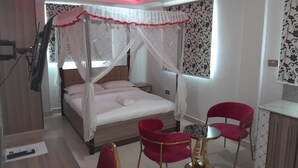 A bedroom with a bed, two red chairs, a small table, and a nightstand. - equine hotel ruiru nairobi (Ruiru)