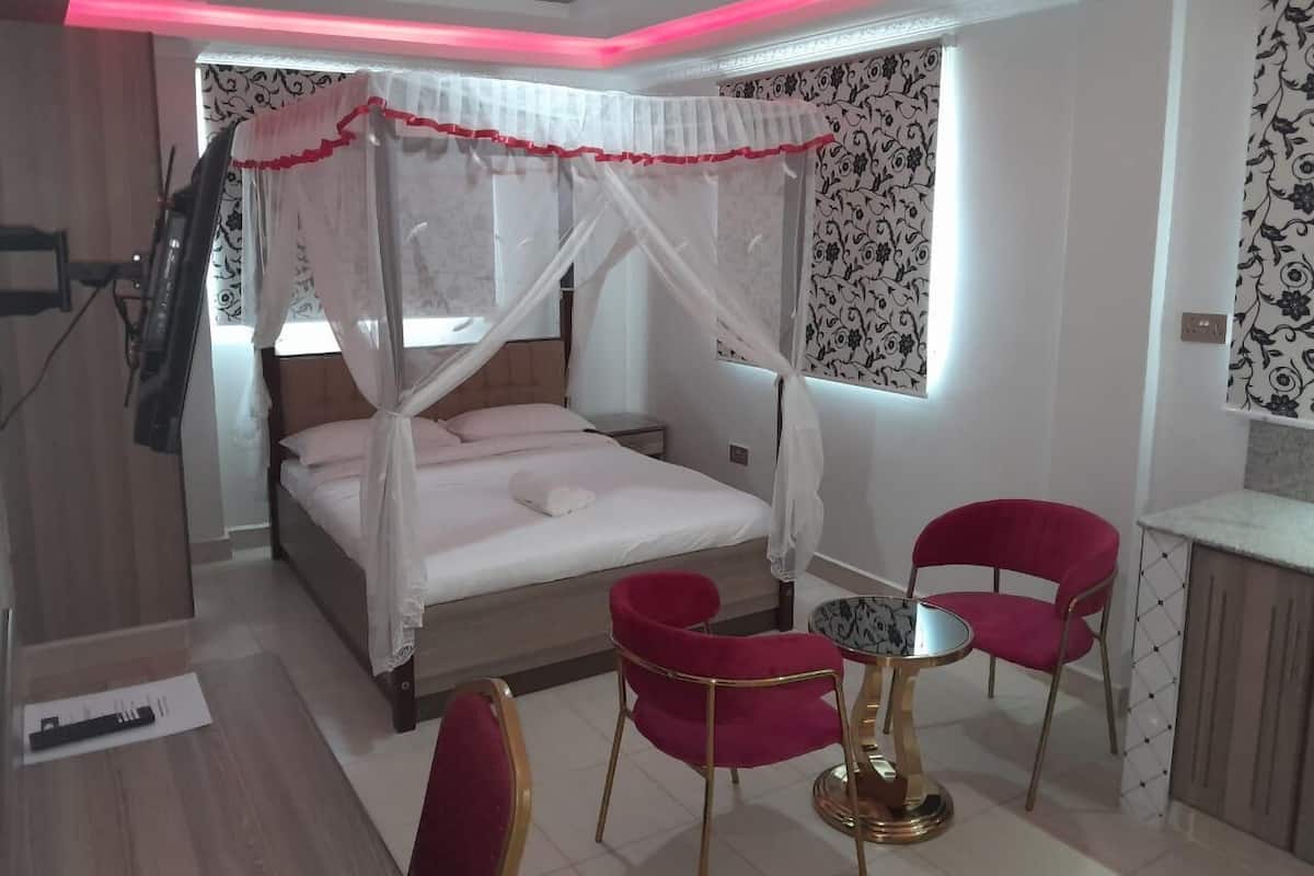 Een slaapkamer met een bed, twee rode stoelen, een klein tafeltje en een nachtkastje.