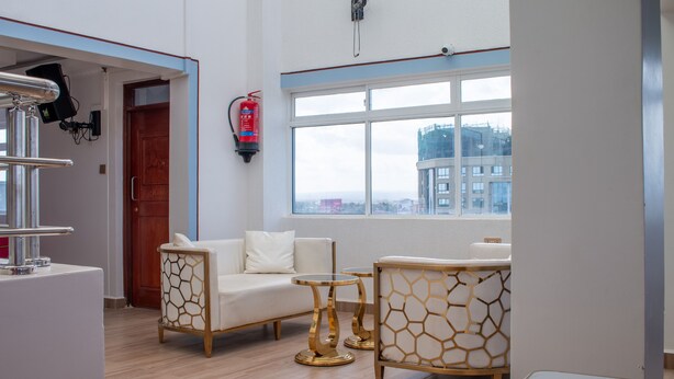 A modern hotel room with a sofa, two gold-framed side tables, a white coffee table, and a large window offering a city view. - equine hotel ruiru nairobi (Ruiru)