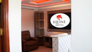 A hotel lobby with a large sign reading "Equine Hotel," a brown leather armchair, wooden shelving, and a tiled wall. - equine hotel ruiru nairobi (Ruiru)