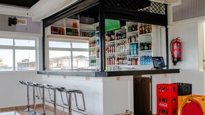 A bar area with a counter, shelves stocked with beverages, a fire extinguisher, and seating with a view of the outside. - equine hotel ruiru nairobi (Ruiru)