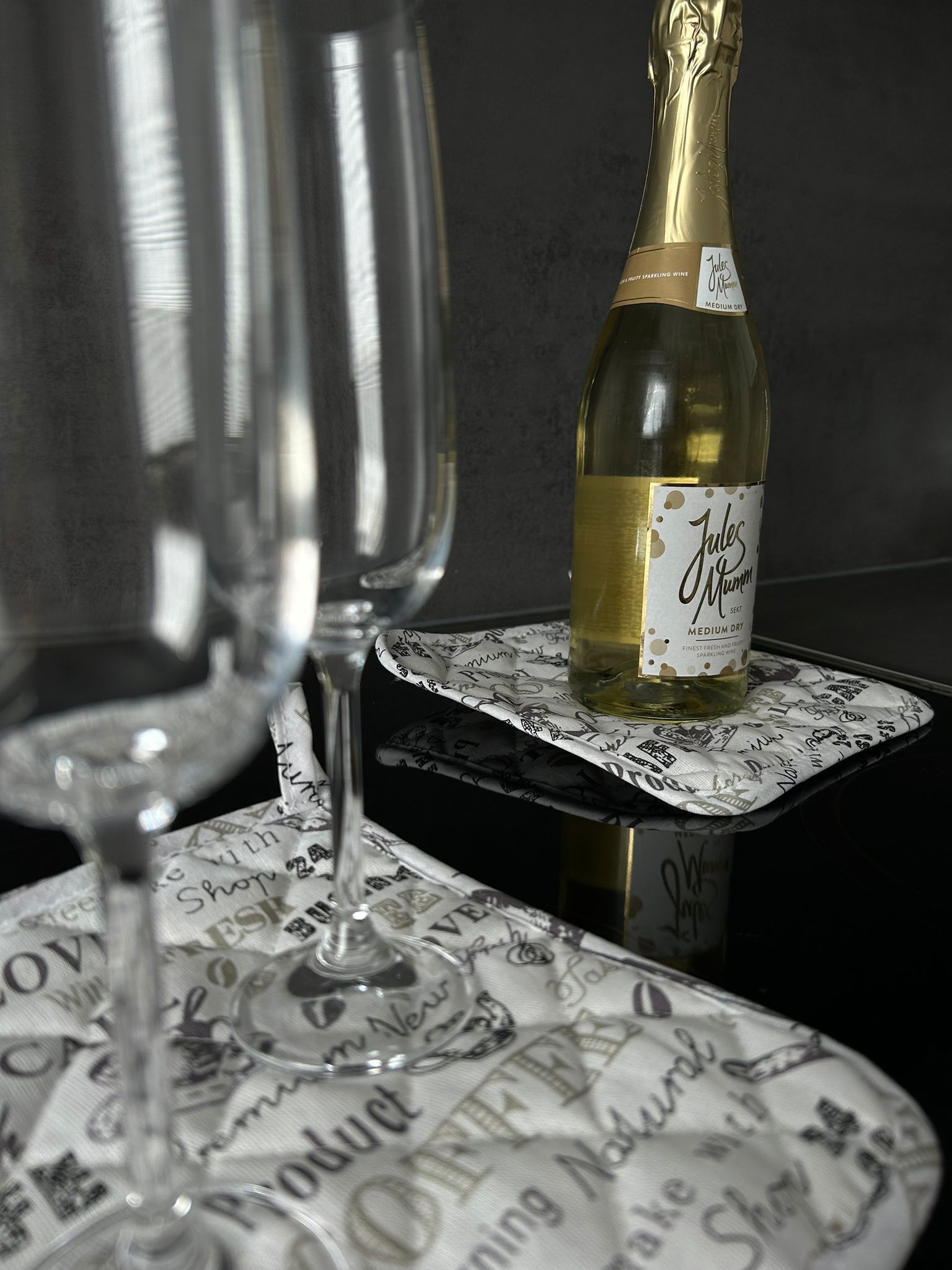 Eine Flasche Jules Mumm halbtrockener Sekt auf einem Tisch mit gemustertem Tischtuch.