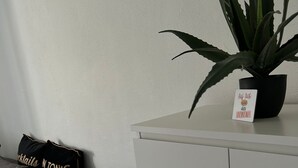 Ein modernes Wohnzimmer mit einem grauen Sofa, einem schwarzen Kissen mit Text, einer weißen Kommode und einer Topfpflanze.