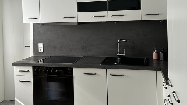 Eine moderne Küche mit weißen Schränken, einer schwarzen Arbeitsplatte und einem eingebauten Backofen.