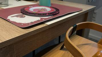 A wooden dining table with a placemat featuring a cartoon character, a teal cup, and a white bowl.