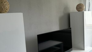 Ein modernes Wohnzimmer mit einem Flachbildfernseher auf einer weißen Unterhaltungseinheit, einer roten Gaming-Konsole und dekorativen Kugeln in Regalen.