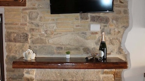 Una chimenea de piedra con repisa de madera, un televisor montado encima y una botella de vino sobre la repisa.