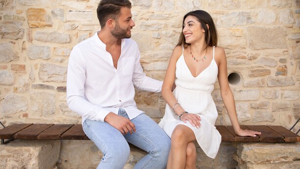 Una pareja sentada en un banco frente a un muro de piedra.