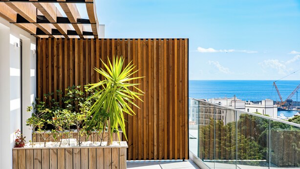 Un balcon avec une balustrade en bois, un pot de fleurs et une vue sur la mer et les bâtiments.