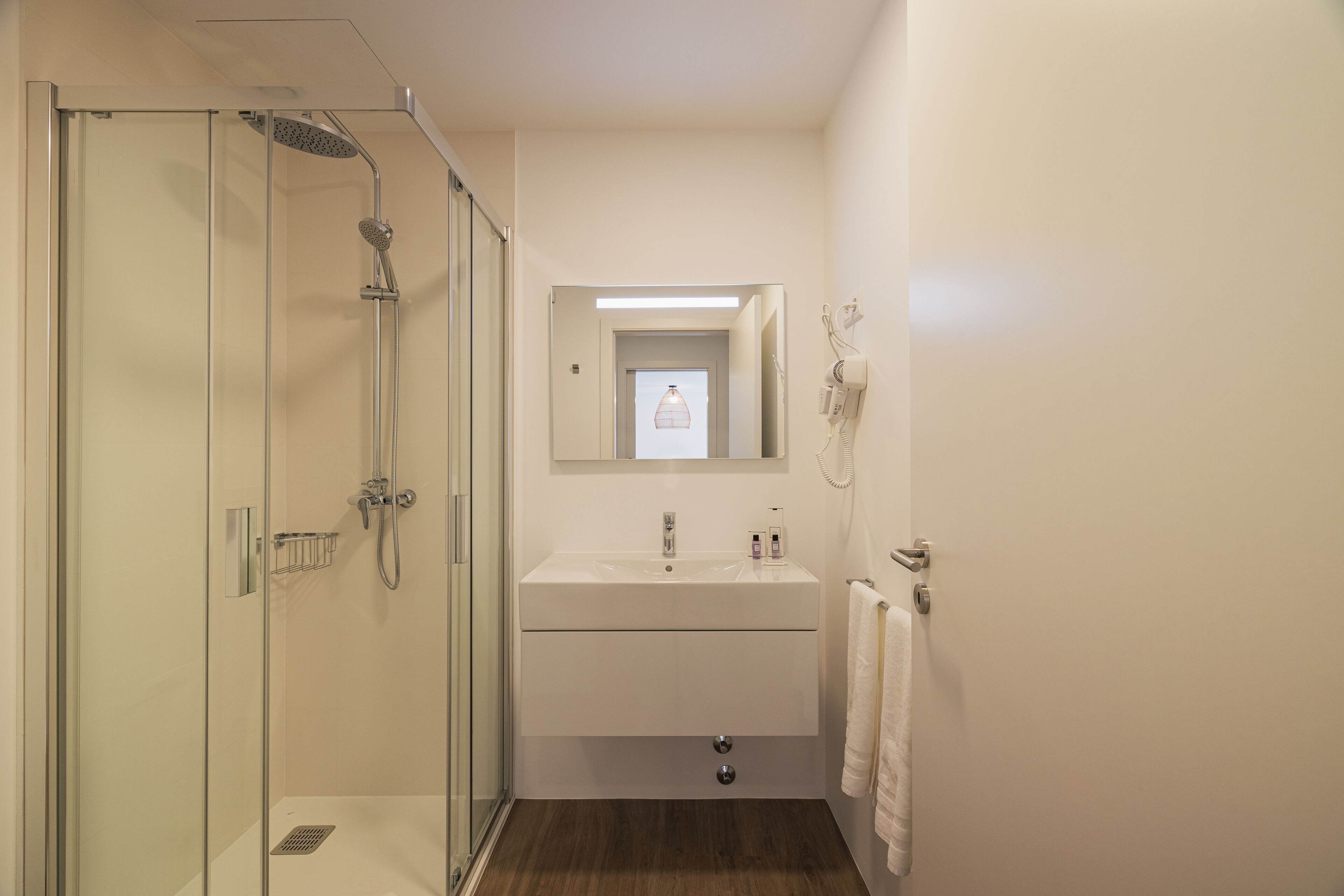 A modern bathroom with a glass-enclosed shower, a white sink, and a mirror above the sink.