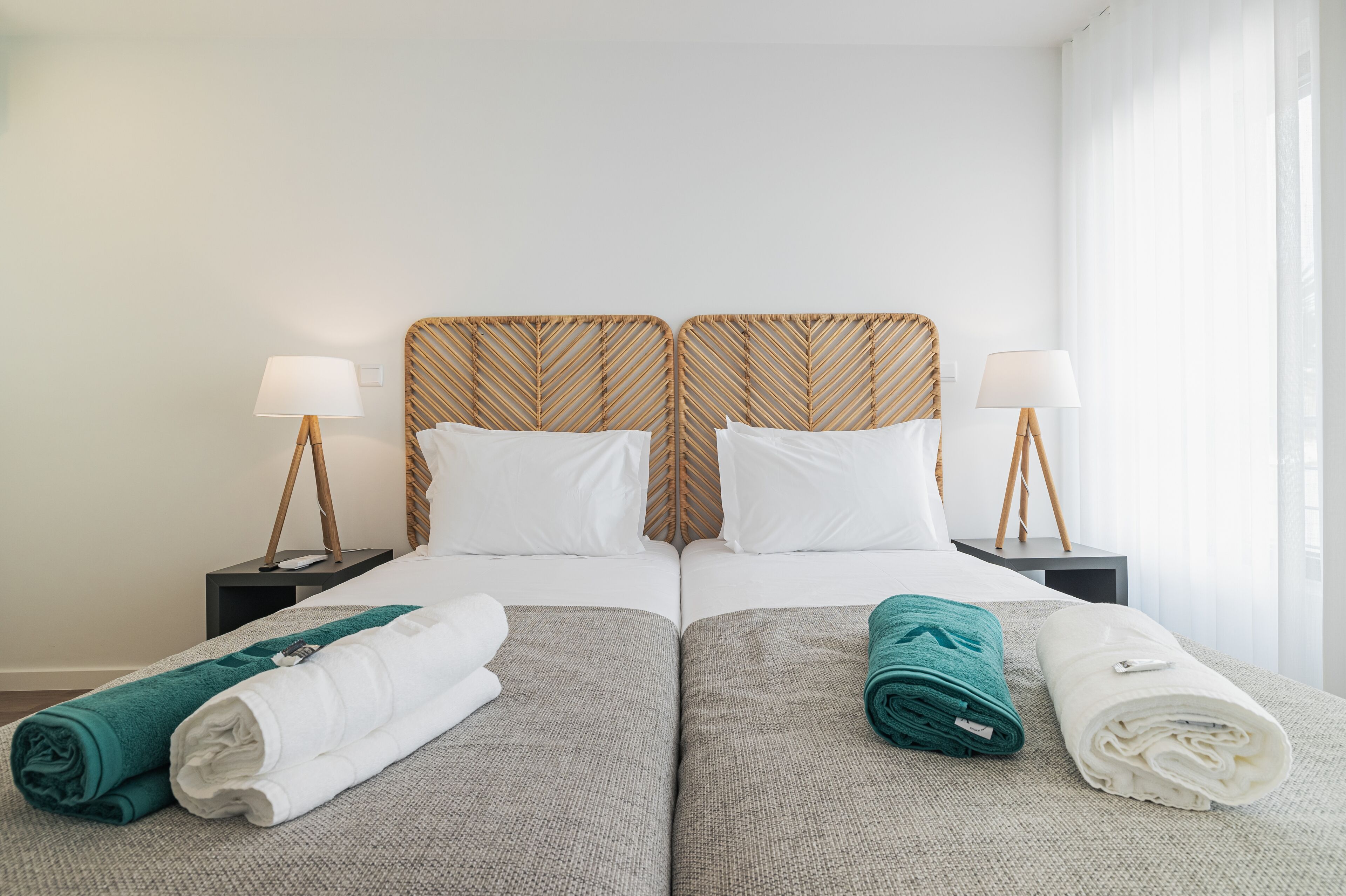 A double bed with a woven headboard, two bedside tables with lamps, and neatly folded towels on the bed.
