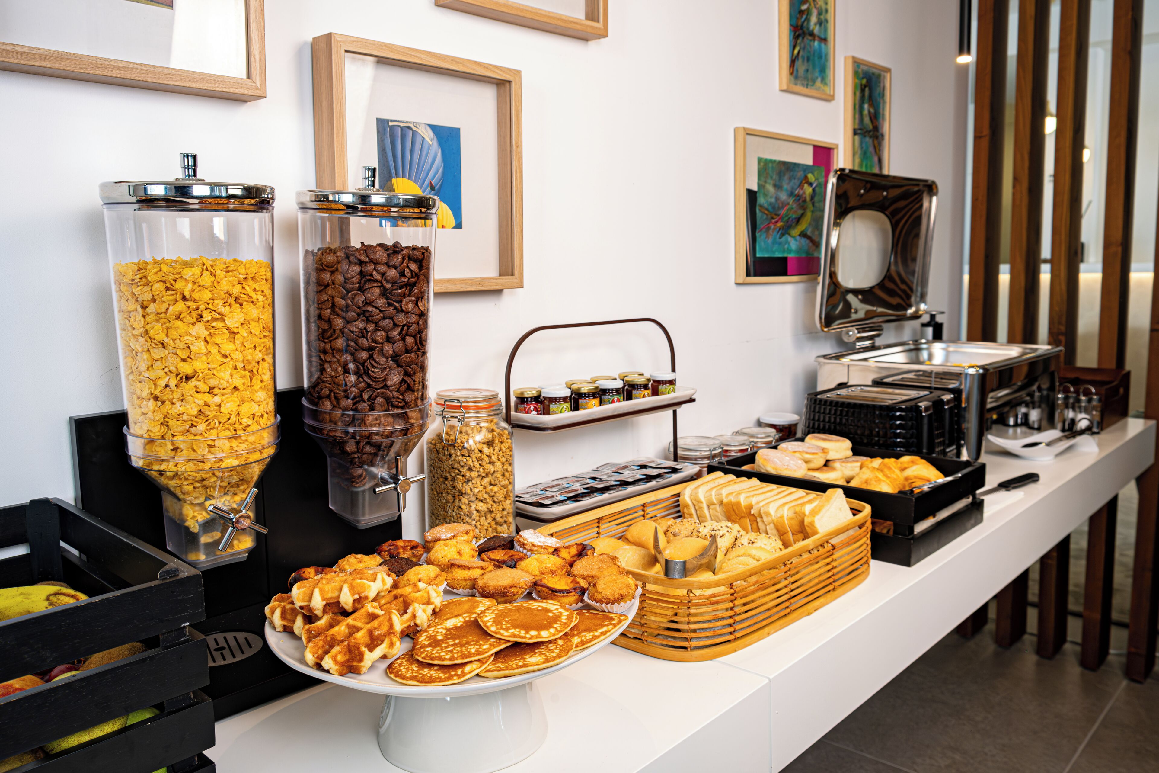 A buffet with various food items, including cereals, coffee, pastries, and bread.