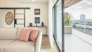 Un salon moderne avec un canapé, un bureau en bois et une vue sur la ville grâce à de grandes fenêtres.