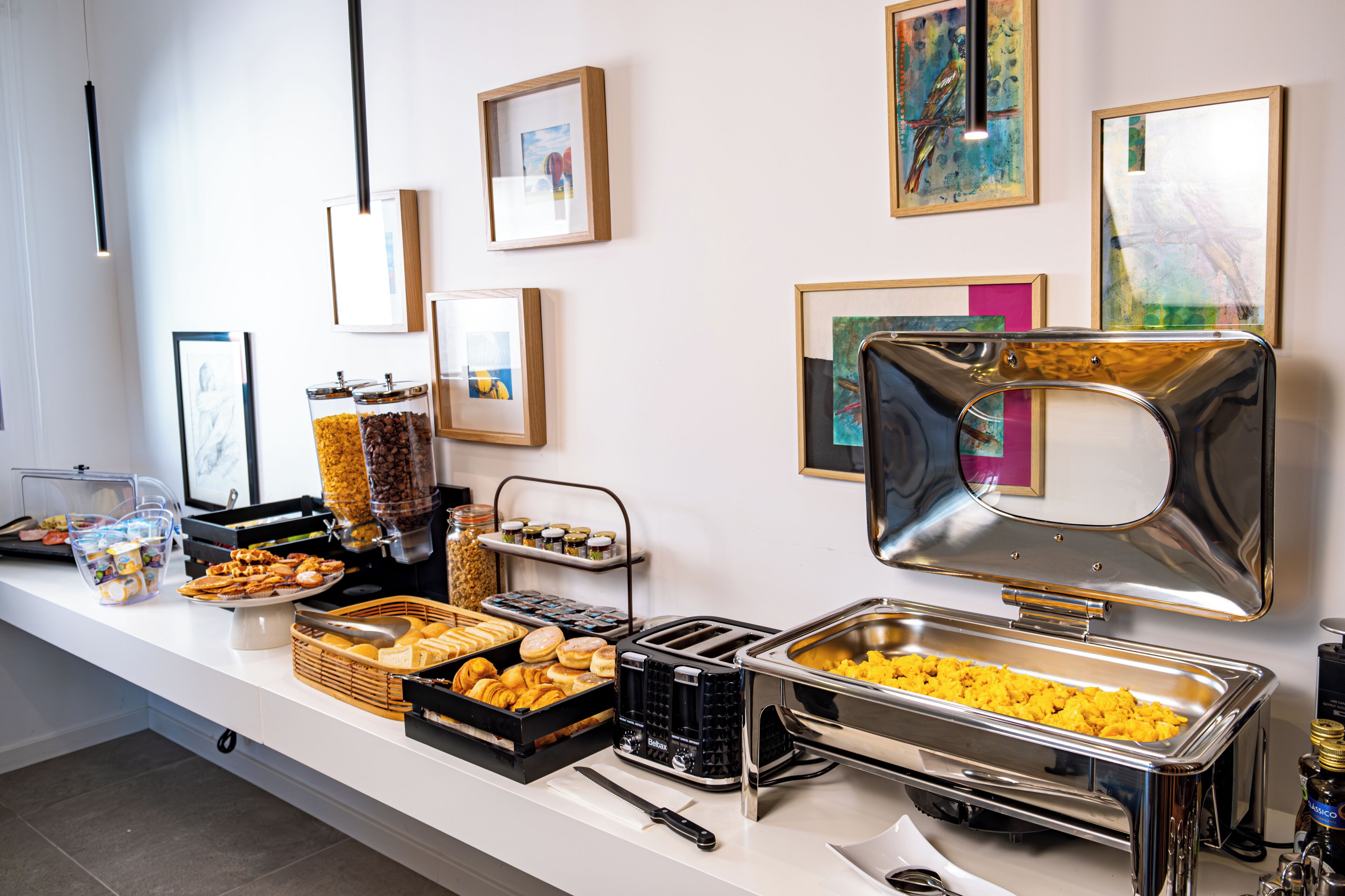 A buffet setup with various food items and condiments, framed artwork on the wall, and a clean, modern counter.