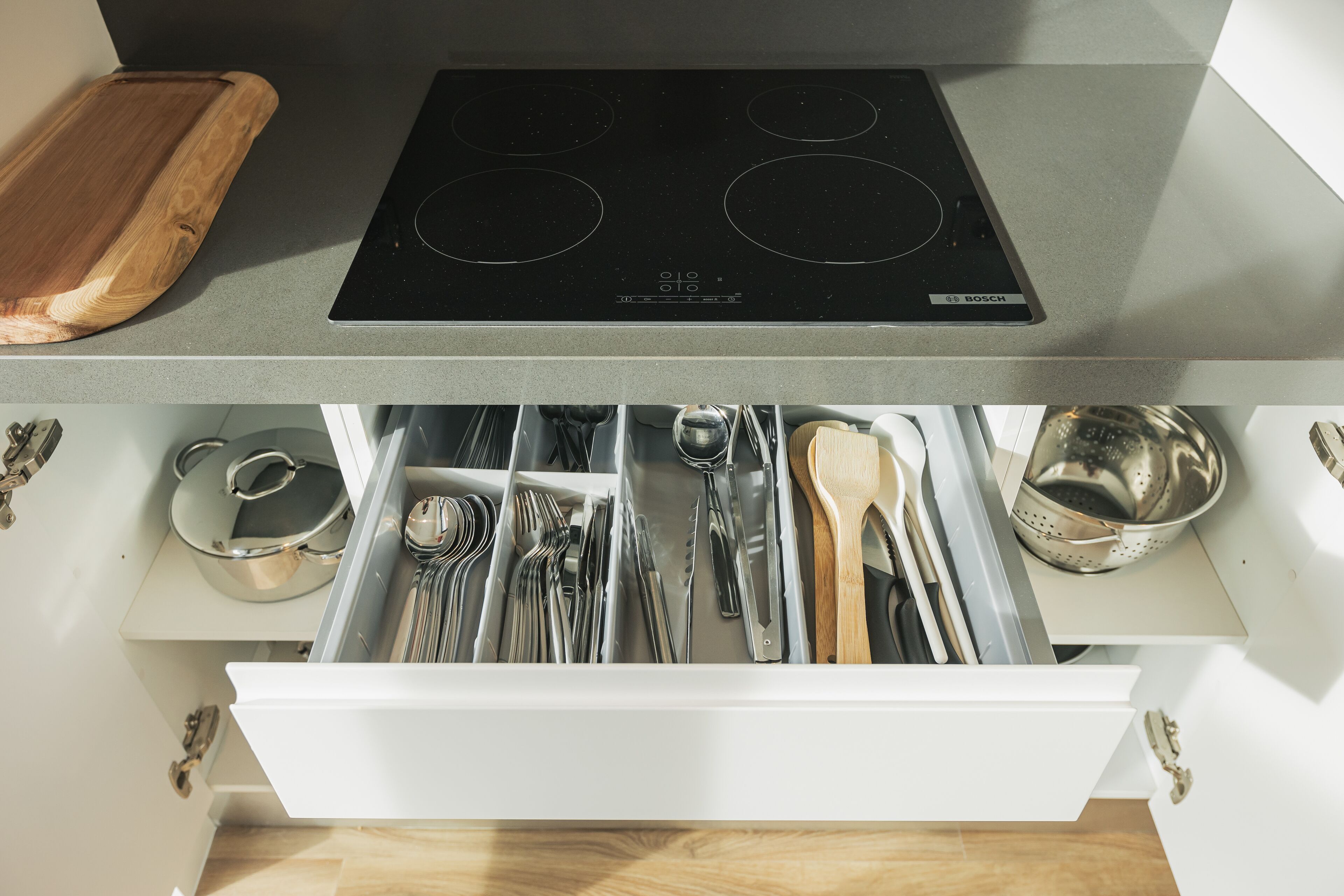 A kitchen with a Bosch induction cooktop, a wooden cutting board, and a drawer organizer with utensils.