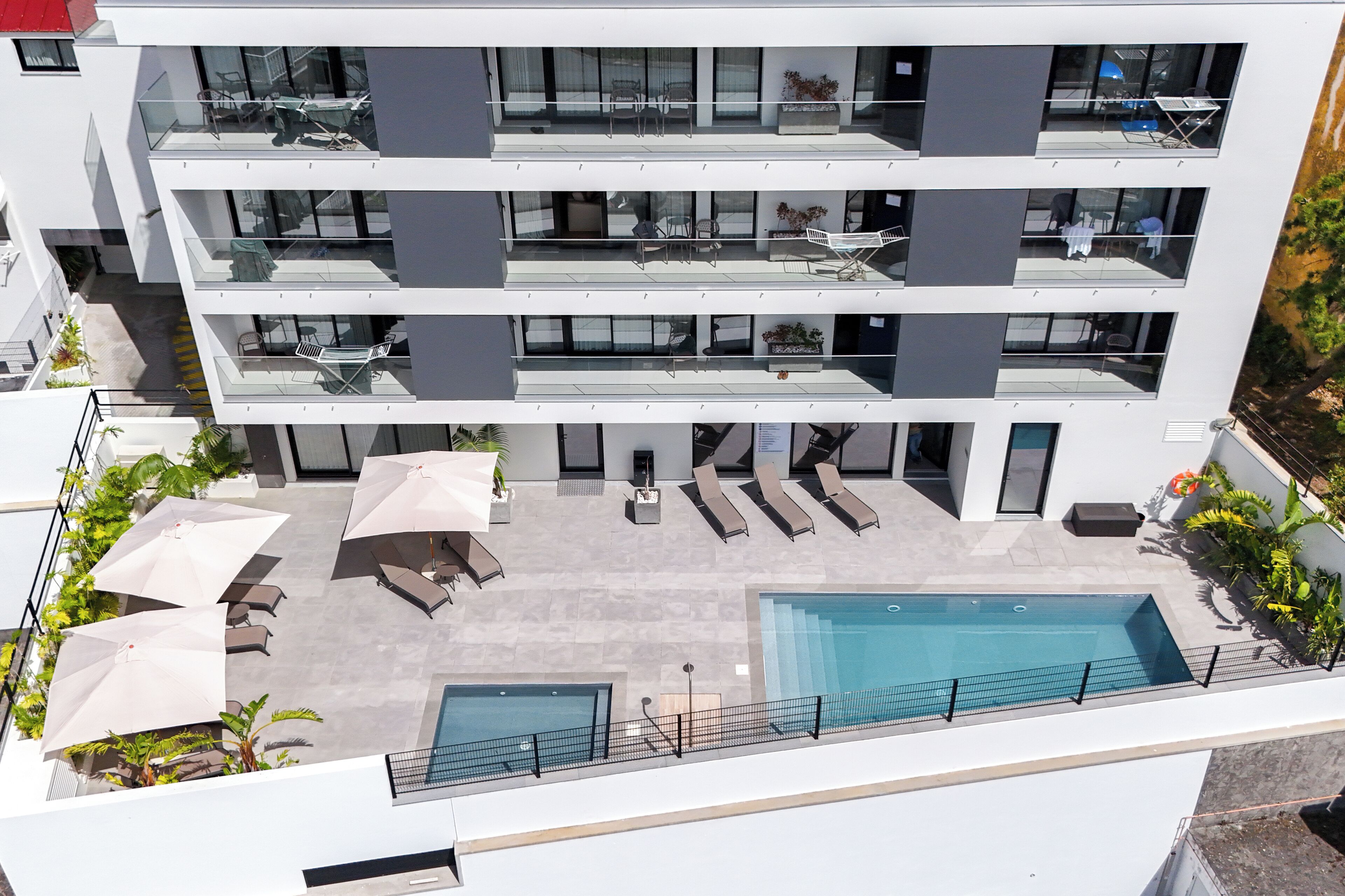 Un edificio moderno de varios pisos con piscina en la azotea, zona de estar al aire libre y balaustrada de vidrio.
