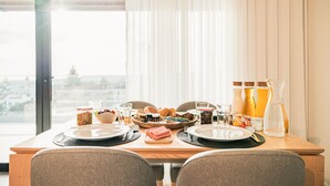 Une table à manger dressée avec des assiettes, des couverts, un saladier de fruits et une bouteille d’eau.
