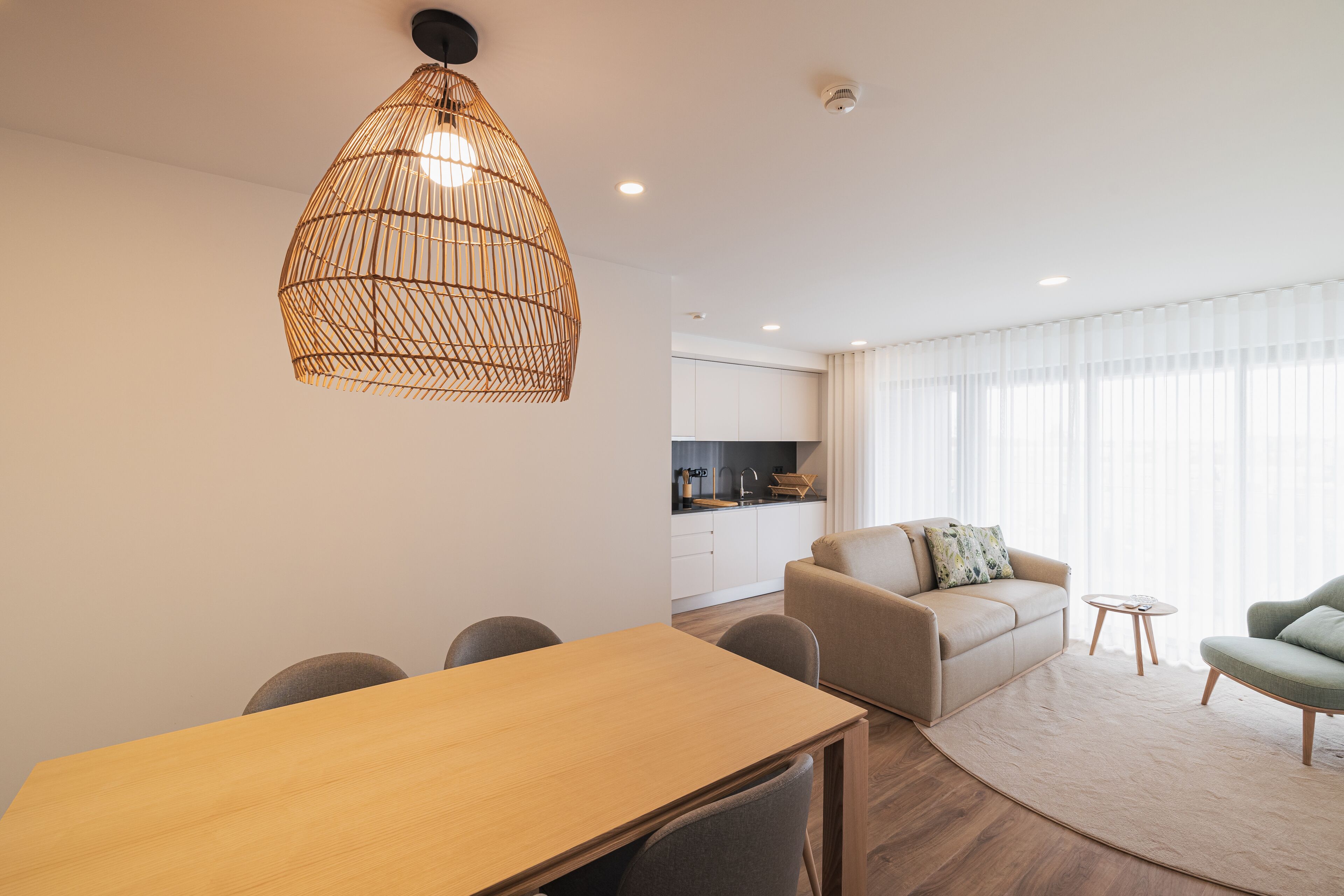 A modern living room with a dining table, sofa, and a kitchen in the background.