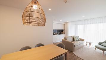A modern living room with a dining table, sofa, and a kitchen in the background.