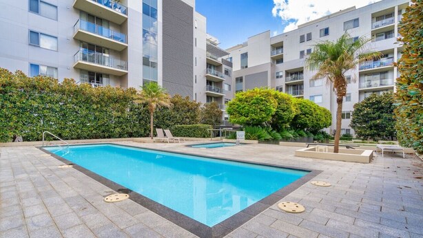 Ein modernes Apartmenthaus mit Schwimmbad, Sitzgelegenheiten im Freien und üppigem Grün.