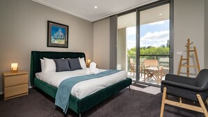Ein Schlafzimmer mit einem großen Bett, einem Nachttisch, einem Sessel und Blick ins Freie durch eine Glasschiebetür.