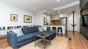 Ein modernes Wohnzimmer mit einem grauen Sofa, einem kleinen Tisch und einer Küchenzeile im Hintergrund.