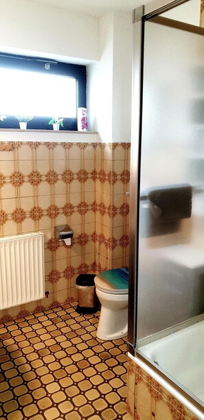 A bathroom with patterned tiles, a toilet, a radiator, and a window with plants. - Ferienhaus mit 4 Wohneinheiten für Gruppen! Hunde Willkommen! (Cuxhaven)