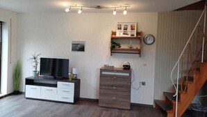 A modern living room with a flat-screen TV, a wooden desk, a bookshelf, and a staircase. - Ferienhaus mit 4 Wohneinheiten für Gruppen! Hunde Willkommen! (Cuxhaven)