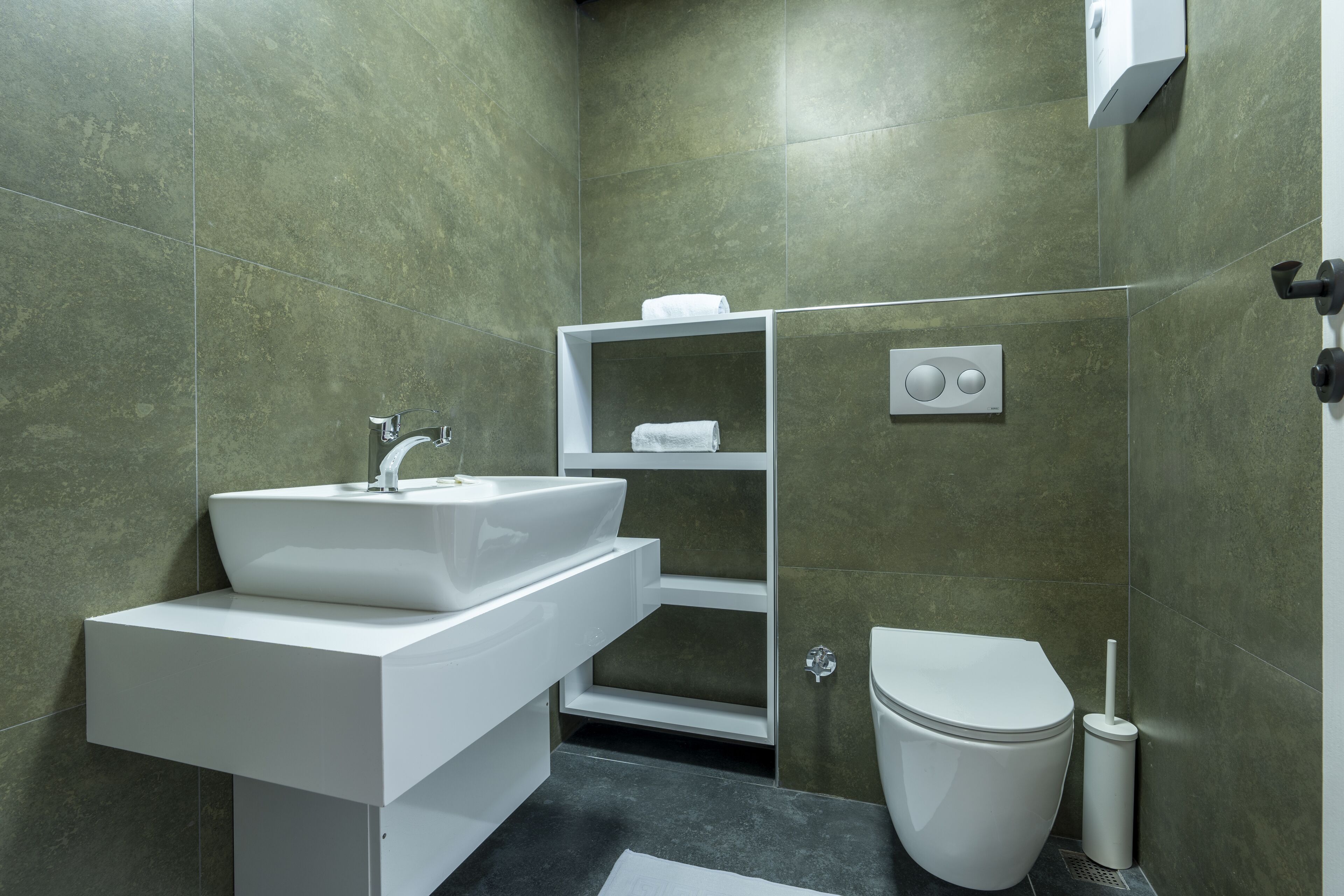 Une salle de bain moderne avec un lavabo blanc, des toilettes et une étagère sur laquelle est posée une serviette.
