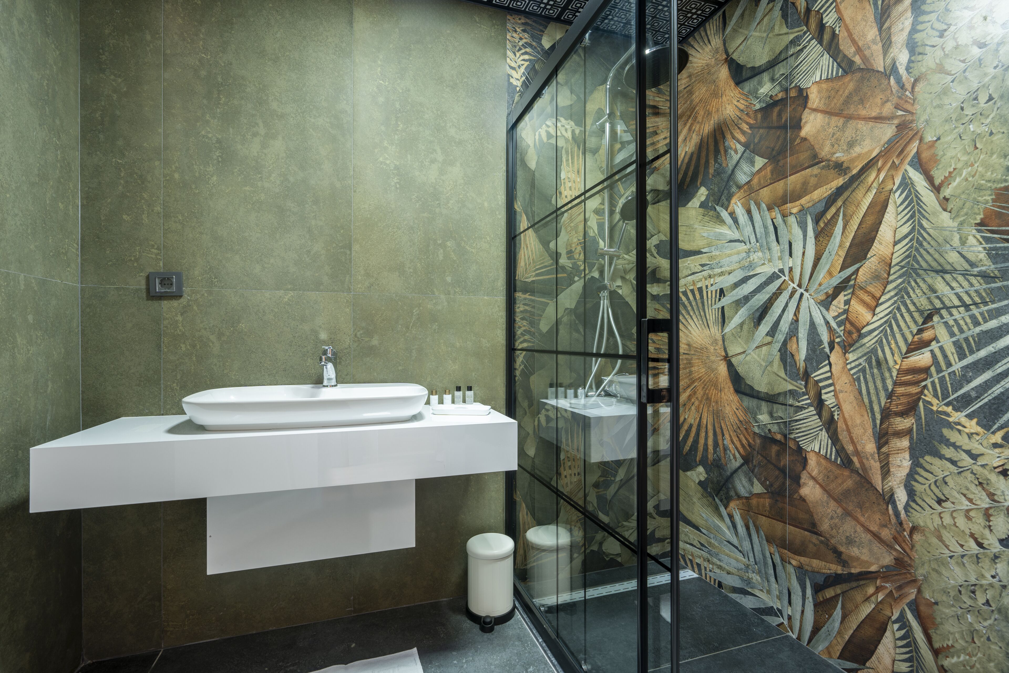 A modern bathroom with a large sink, a glass shower enclosure, and a green-tiled wall.