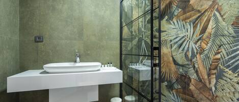 A modern bathroom with a large sink, a glass shower enclosure, and a green-tiled wall.