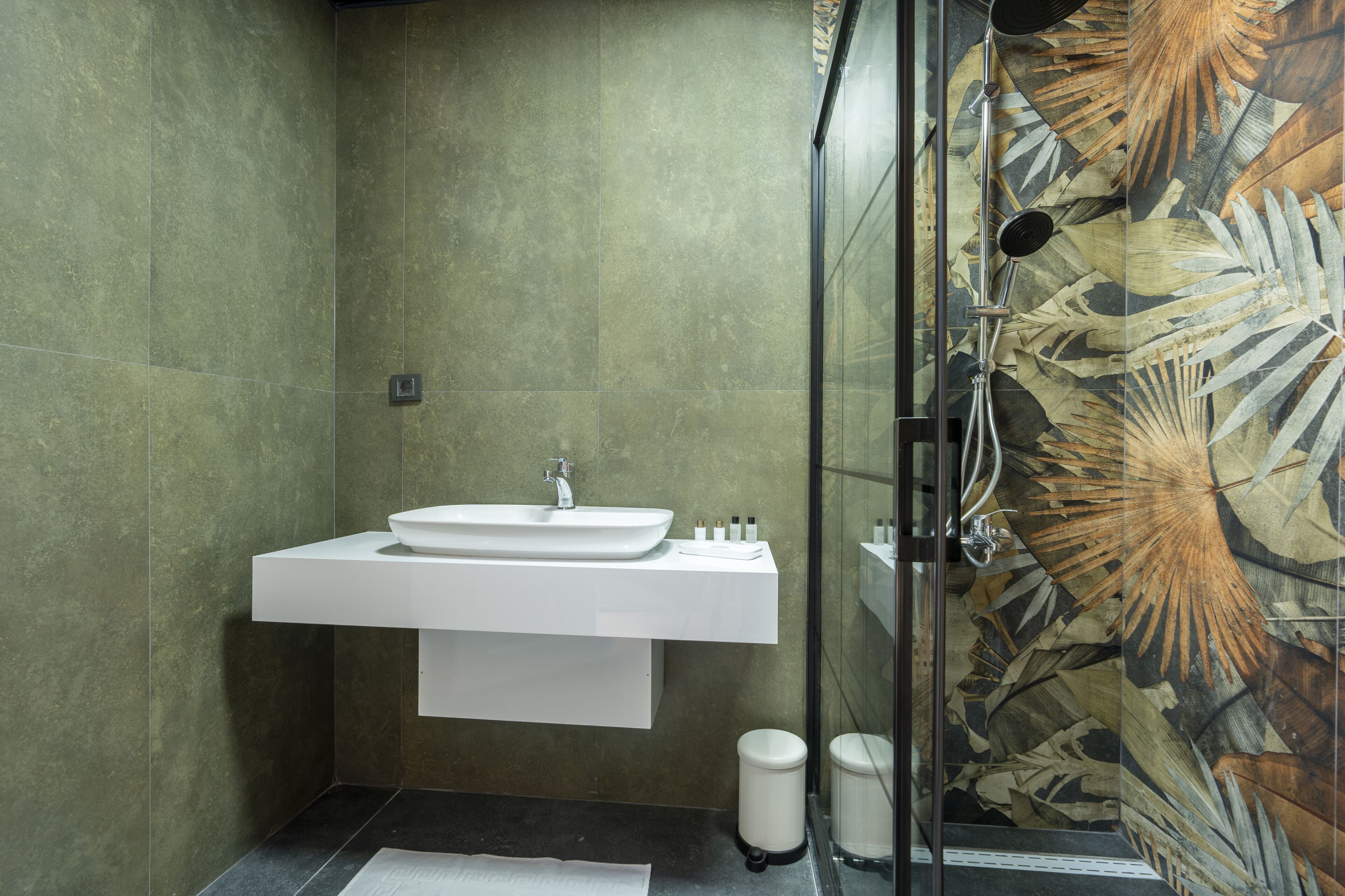 Ein modernes Badezimmer mit einem weißen Waschbecken, einer Duschkabine aus Glas und einer Wand mit einem dekorativen Blattmuster.