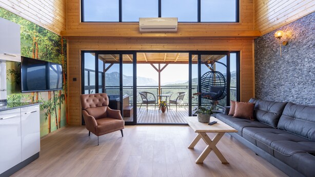 A spacious living area with a large sliding glass door leading to an outdoor terrace, a modern kitchen, and a cozy seating area with a sofa and armchair. - La Veranda Villas (Kumluca)