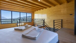 A wooden cabin room with a bed, towels, a window with a view of mountains, and a balcony with a railing. - La Veranda Villas (Kumluca)