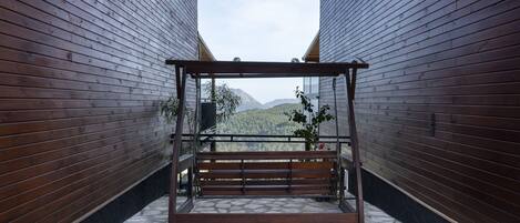 Un banco de madera con estructura metálica en un estrecho pasillo con suelo de piedra y vistas a montañas.