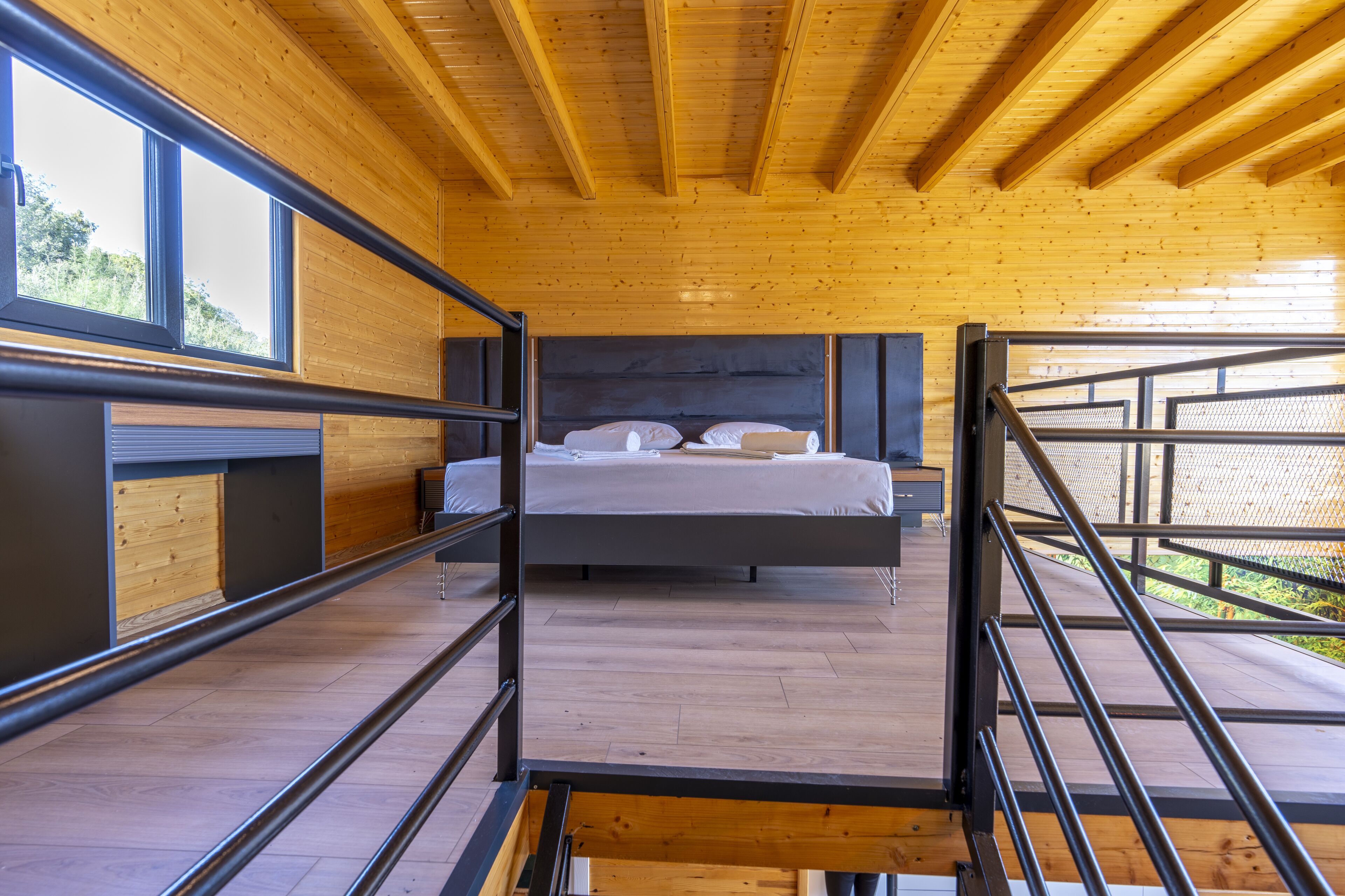 A modern bedroom with a large bed, wooden ceiling, and a view of the outdoors through large windows.