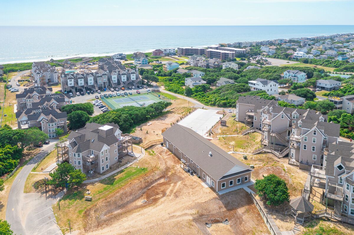 An aerial view of a coastal residential area with houses, a tennis court, and a large building under construction.