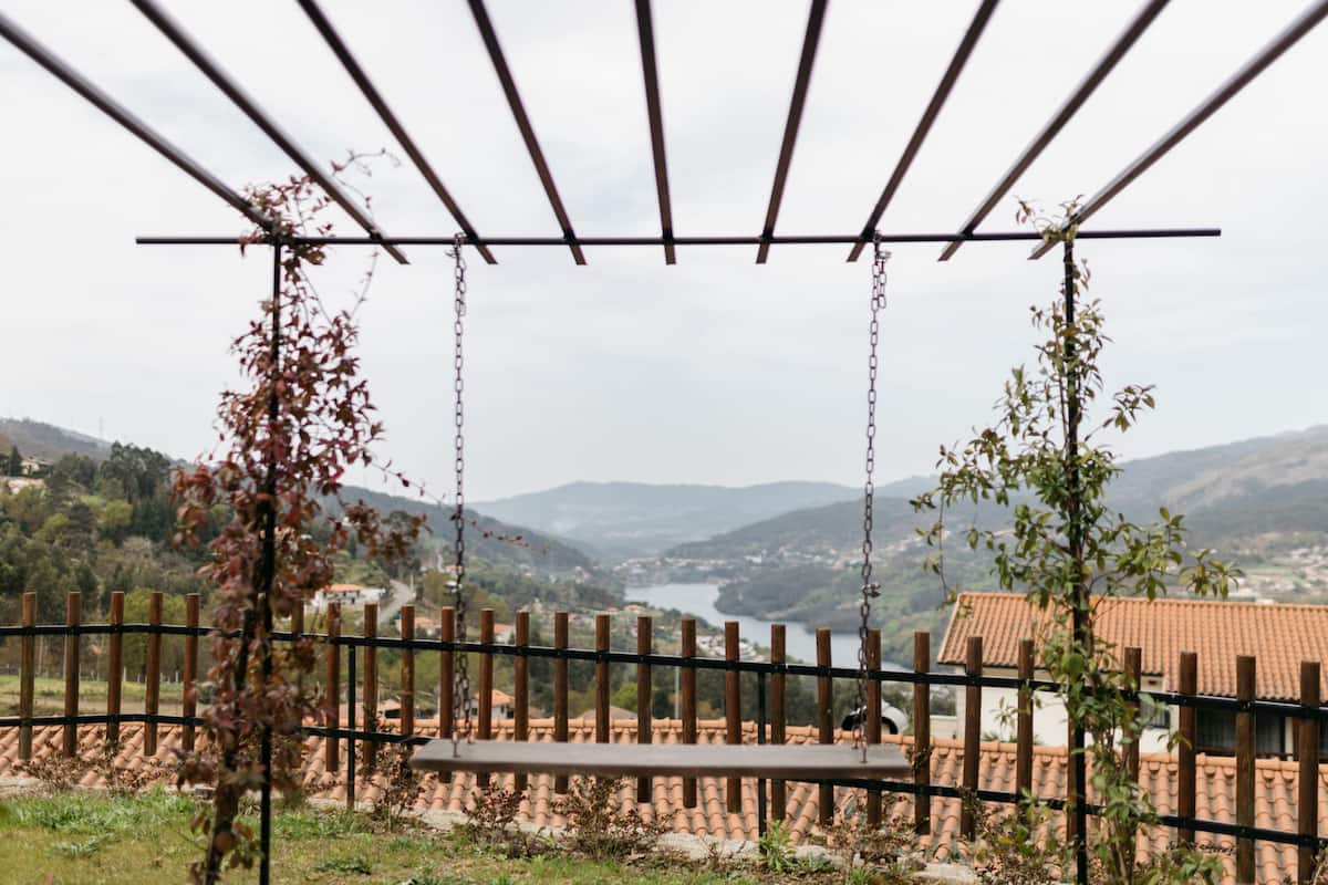 Un columpio de madera con vistas a un lago y montañas al fondo.